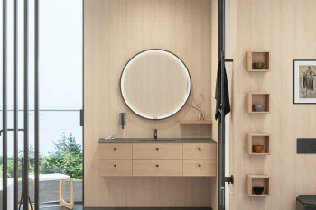 Minimalist interior with light wood walls, floating six-drawer vanity, black countertop, and round backlit mirror; glass divider and outdoor greenery visible.