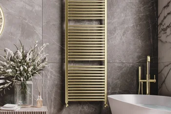 Luxurious bathroom with a gold towel radiator on dark marble walls, a white freestanding tub with a gold faucet, and a slatted cabinet with dried flowers.