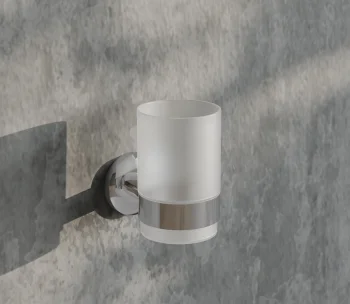 Chrome wall-mounted frosted glass tumbler holder with cylindrical frosted glass cup on a round metal mount against a textured grey wall.