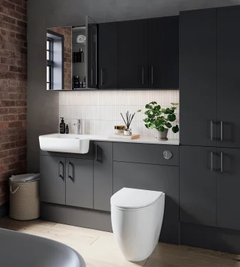 Modern bathroom with dark grey cabinetry, white sink and toilet, white tiled splashback, brick wall and a large window, plus a potted plant on the counter.