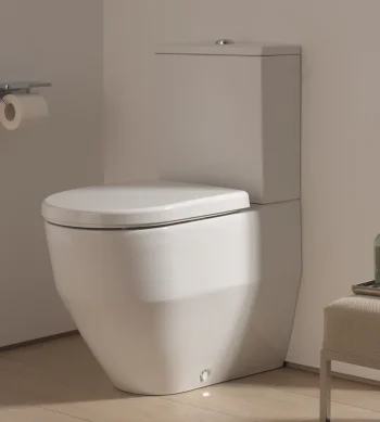 Modern white toilet in a neutral beige bathroom, with a wall-mounted toilet paper holder and a small tray of lotion bottles on a bench beside it.