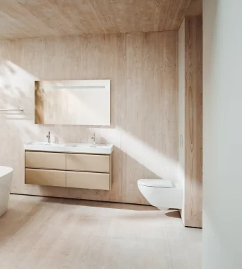 Bright bathroom with light wood panels, a white freestanding tub, beige floating vanity with double sinks, and a glass wall with a tree outside.