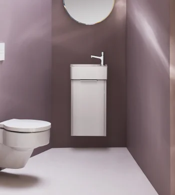 Minimalist bathroom with purple walls, a wall-mounted toilet on the left, a slim white vanity sink on the right, and a round mirror above.