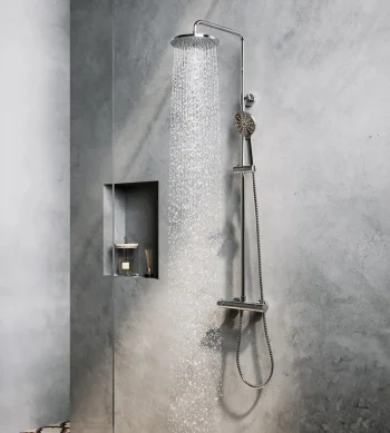 Concrete grey bathroom with a tall rain shower on the right, a handheld unit and hose; a recessed niche holds a candle and diffuser; a towel and small bag hang on the left.