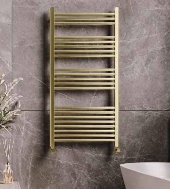 Luxurious bathroom with a gold towel radiator on grey marble walls, a white freestanding tub with gold fixtures, and a vase of white flowers on a wooden surface.