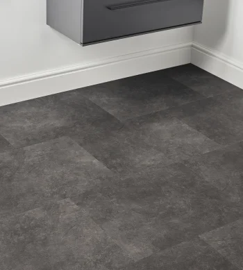 Dark grey stone-look floor tiles in a white room corner, with a floating grey cabinet above and a black towel rack to the right.