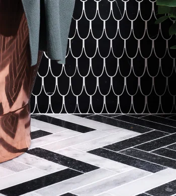 Corner of a room with a black wall featuring a white scallop pattern, copper drape on the left, grey fabric, a potted plant, and a black-and-white chevron floor.