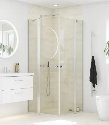 Bright modern bathroom with circular backlit mirror, white vanity with two drawers, glass-framed shower, toilet, and a plant by the window.