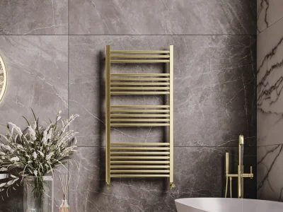 Luxurious bathroom with grey marble walls, a gold ladder towel warmer, a white freestanding tub with gold fixtures, and a vase of white flowers on a wooden surface.