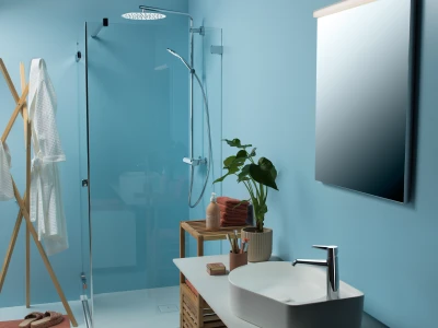 Modern bathroom with blue walls, glass shower enclosure and rainfall head, white basin sink with chrome tap, wooden rack with towels and a plant.