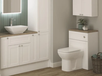 White bathroom with wooden worktops, square vessel sink, backlit mirror, green paneled wall, and toilet; decorative plant and wicker basket nearby.