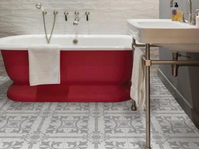 Red tub with white interior in a tiled bathroom, white towel over its edge, chrome fixtures, and a white sink with patterned floor tiles.