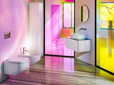 Vibrant modern bathroom display with wall-hung toilet and bidet, a floating vanity sink, pink-green-yellow tinted glass walls, circular wall mirror, and a striped floor.