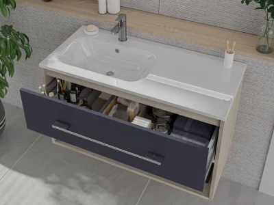 Modern bathroom vanity with a white sink and chrome tap; a dark blue drawer is pulled open, revealing bottles, brushes and towels inside.