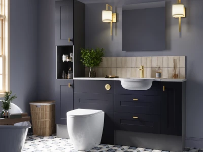 Modern navy bathroom with gold hardware, white basin, matching vanity, beige tile backsplash, wall sconces, plant, wicker hamper and patterned floor.