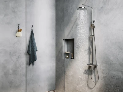 Concrete grey bathroom with a tall rain shower on the right, a handheld unit and hose; a recessed niche holds a candle and diffuser; a towel and small bag hang on the left.