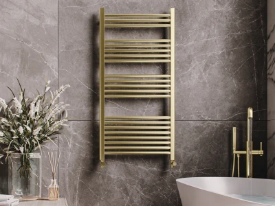 Luxurious bathroom with a gold towel radiator on grey marble walls, a white freestanding tub with gold fixtures, and a vase of white flowers on a wooden surface.