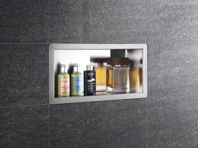 Recessed stainless shelf in dark tile wall with two green L’Occitane bottles, a Biotherm Homme bottle, and a Dolce & Gabbana perfume.