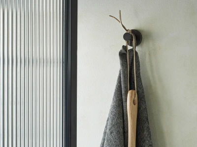 Grey herringbone coat on a round wall hook with a wooden oar and rope, mounted on a pale green wall beside a vertical corrugated metal panel.
