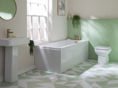 Bright bathroom with a white pedestal sink, freestanding bathtub and toilet, pale green ribbed wall panels, mint and white geometric tiled floor, round mirror, window and plants.