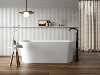 Minimalist bathroom with a white freestanding tub, black floor tap, wood floors, textured white wall, table with dried stems, and beige curtains.