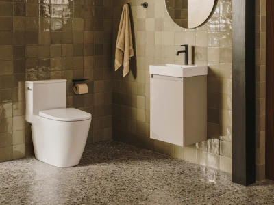 Contemporary bathroom with beige tiled walls, white toilet and a wall-mounted vanity with sink; round mirror, beige towel, and a speckled terrazzo floor.