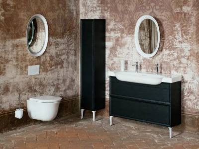 Bathroom with a white sink on a dark vanity, a tall black cabinet, two round mirrors, and a wall-mounted toilet against distressed brown wallpaper.