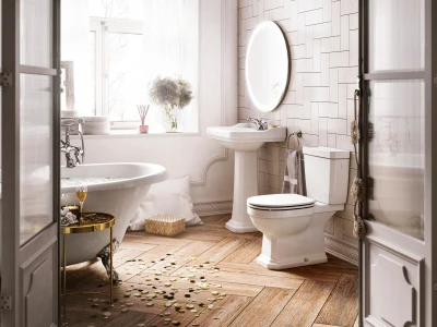 Bright vintage bathroom with a white freestanding tub, pedestal sink and toilet; round mirror, window light, and petals scattered on the wooden floor.