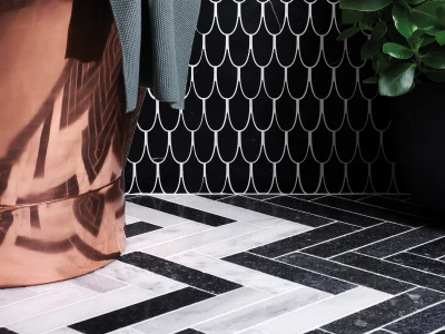 Corner of a room with a black wall featuring a white scallop pattern, copper drape on the left, grey fabric, a potted plant, and a black-and-white chevron floor.