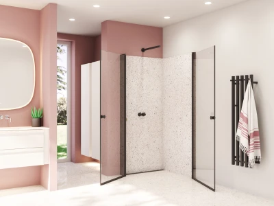 Modern pink bathroom with terrazzo shower walls, glass doors with dark frames, white vanity with a rounded mirror, and a black towel rail with a striped towel.