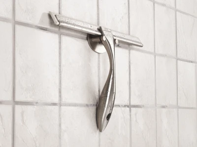 A chrome curved metal lever mounted on a circular backplate, attached to a horizontal rail on a white tiled wall.