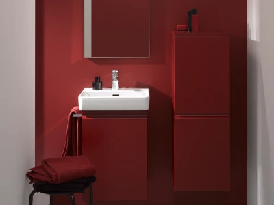 Contemporary bathroom with a white rectangular sink on a red vanity, chrome tap, and tall red cabinets. Red towels sit on a stool beside the sink.