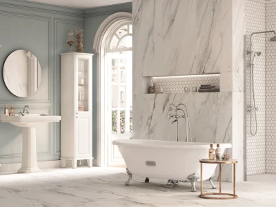 Luxurious marble bathroom with a freestanding clawfoot tub, pedestal sink, round mirror, tall glass-front cabinet, arched window, and hex-tiled shower.