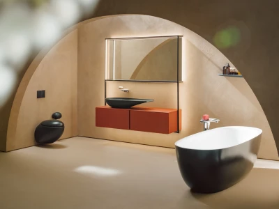 Minimalist bathroom with curved beige walls, a black freestanding tub, orange wall-mounted vanity with a black vessel sink, a backlit mirror, and a stool.