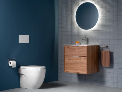 Modern bathroom with a teal wall, wall-hung toilet, dual-flush plate, wooden vanity, circular backlit mirror, chrome tap, and a brown towel.