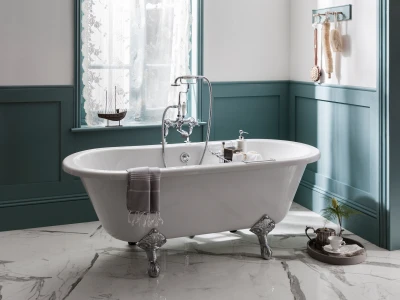 White clawfoot bathtub with chrome fittings in a teal panelled bath. Lace window, sailboat on the sill, bath products, towel over edge, and a tea set.