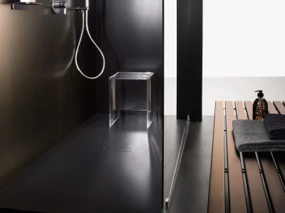 Modern black shower area with a round rain head and handheld shower, chrome fixtures, a clear acrylic stool, and a wooden slatted bench with towels.