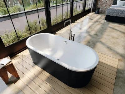 Freestanding white tub with chrome tap in a glass-walled bathroom, wooden deck, and a bed visible in the background.