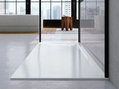 Modern interior with glass walls and city skyline view; white rectangular shower tray in the foreground, grey seating to the left, and a wooden stool.