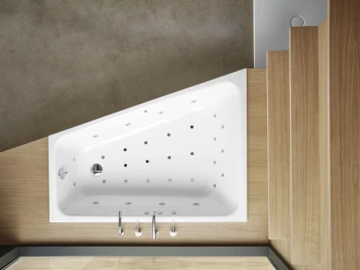 White rectangular whirlpool bathtub with numerous jets and chrome taps, set in a light wood surround with stepped panels against a concrete wall.