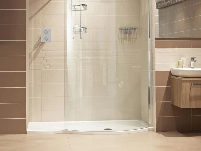 Modern bathroom with a curved glass shower, rainfall head, chrome shelves, beige and brown tiled walls, and a wooden vanity with sink.
