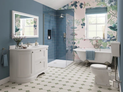 Bright bathroom with blue walls, white vanity, glass shower, blue tiles, floral wallpaper by a window, freestanding tub and toilet; patterned floor.