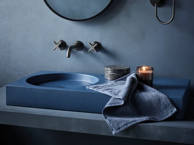 Blue bathroom with a circular sink set into a vanity, wall-mounted taps, a folded towel, and a lit candle beside a marble container on the counter.