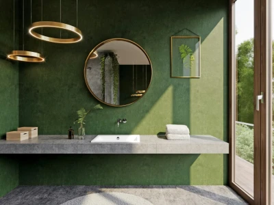 Modern bathroom with green textured wall, concrete counter, white sink, round gold mirror, ring lights, plants, towels, and a glass door to greenery.