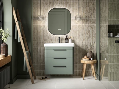 Green bathroom vanity with white top and rounded mirror, beige tile wall, glass globe lights, a wooden ladder, plant, slippers and a stool with bottles.