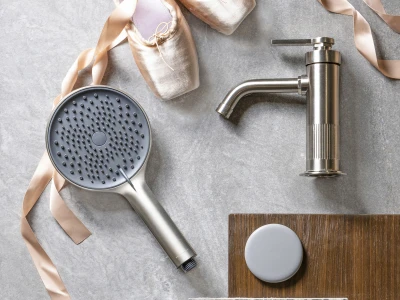 Ballet pointe shoes with pale pink ribbons, a metal handheld shower head and faucet, and tile samples arranged on a wooden board.