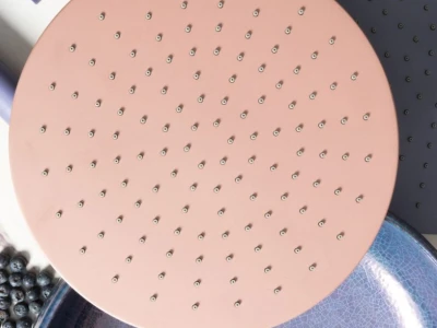 Top-down view of a peach-pink perforated round board on a blue plate, with a small pink disk nearby and blueberries along the edge on a marble surface.