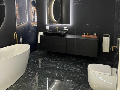 Modern black bathroom showroom with a freestanding white tub, dark vanity, backlit oval mirror, gold fittings and marble floors.