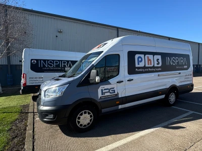 White commercial van with PBS Inspira branding on its side, parked in a parking lot beside a grey industrial warehouse on a sunny day.