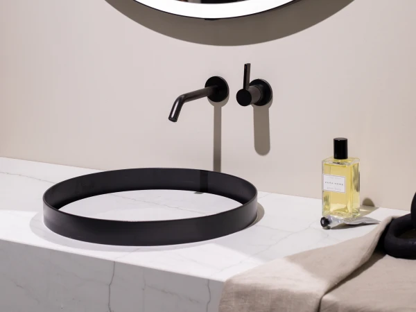 Round black basin on white marble counter under a mirror; black faucet and lever, with a yellow liquid soap bottle and a beige towel.